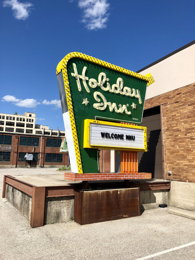 Holiday Inn-Schriftzug an einem Gebäude mit einem Textschild davor, bewölkter Himmel und sichtbare Fenster.