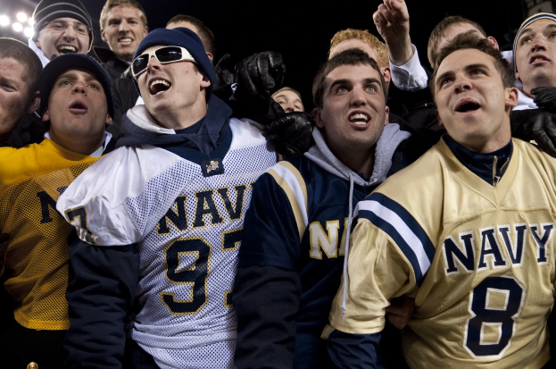 Fans der Navy-Footballmannschaft jubeln ihrem Team während eines Spiels unter Stadionbeleuchtung zu.