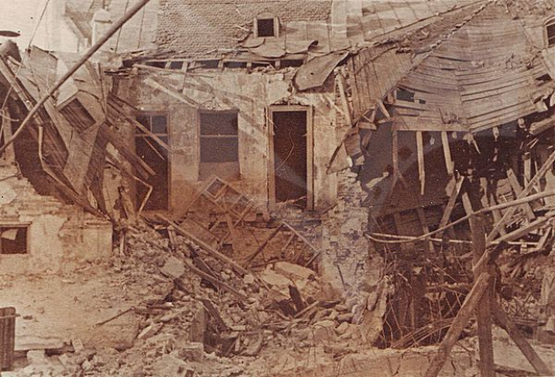 Ein altes Schwarz-Weiß-Foto eines baufälligen Gebäudes mit zerbrochenem Holz, bröckelnden Wänden und zerschlagenen Fenstern und Türen.