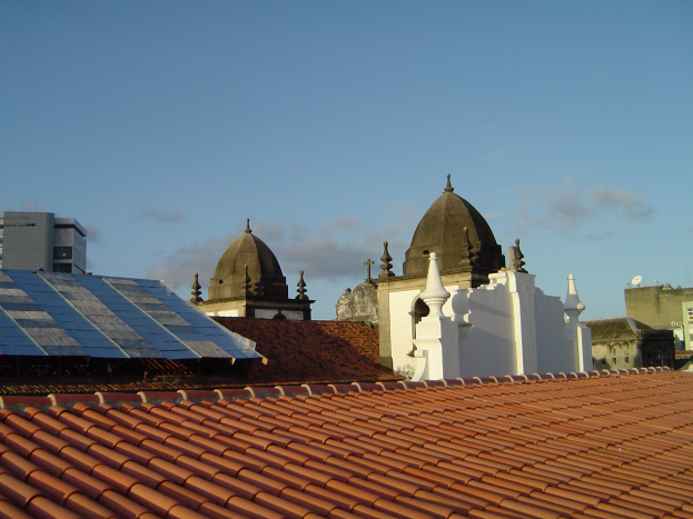 Stadtansicht mit Gebäuden im Vordergrund, einem blauen Himmel im Hintergrund und Solarpanels auf einem Dach.